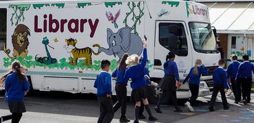 A photograph of a mobile library vehicle. Children run past it.