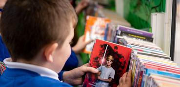 A schoolboy smiles as he looks at the cover of a book in a library.